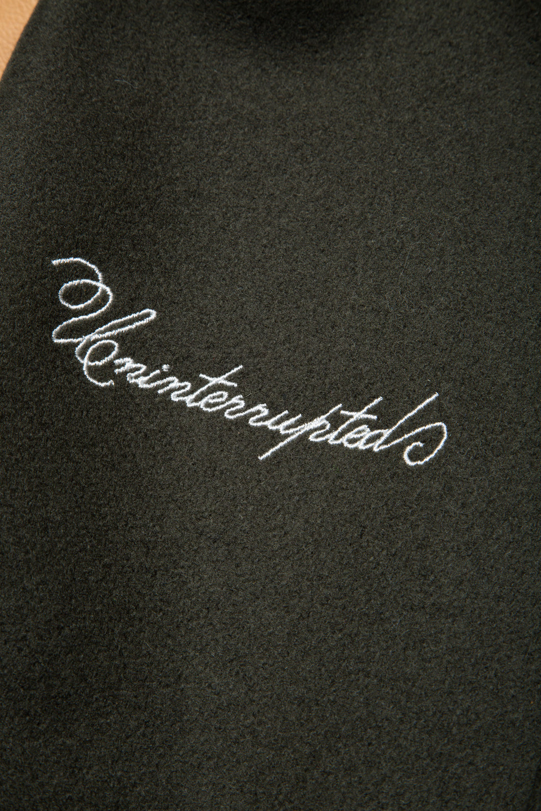 UNINTERRUPTED ALL STAR VARSITY JACKET LODEN GREEN (4458685071440) - close up of the "uninterrupted" embroidery